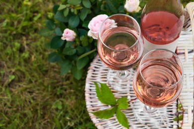 Photo of Glasses and bottle of delicious rose wine on picnic basket outdoors. Space for text