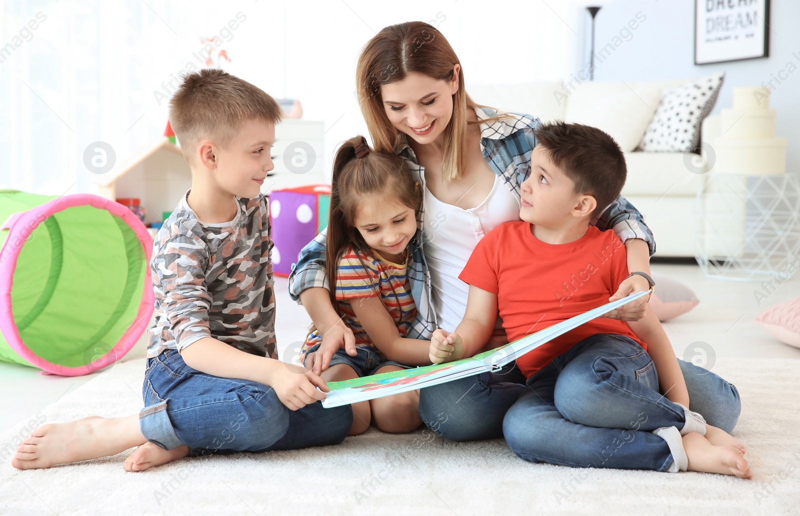 Photo of Cute little children reading book on floor with young mother in playing room