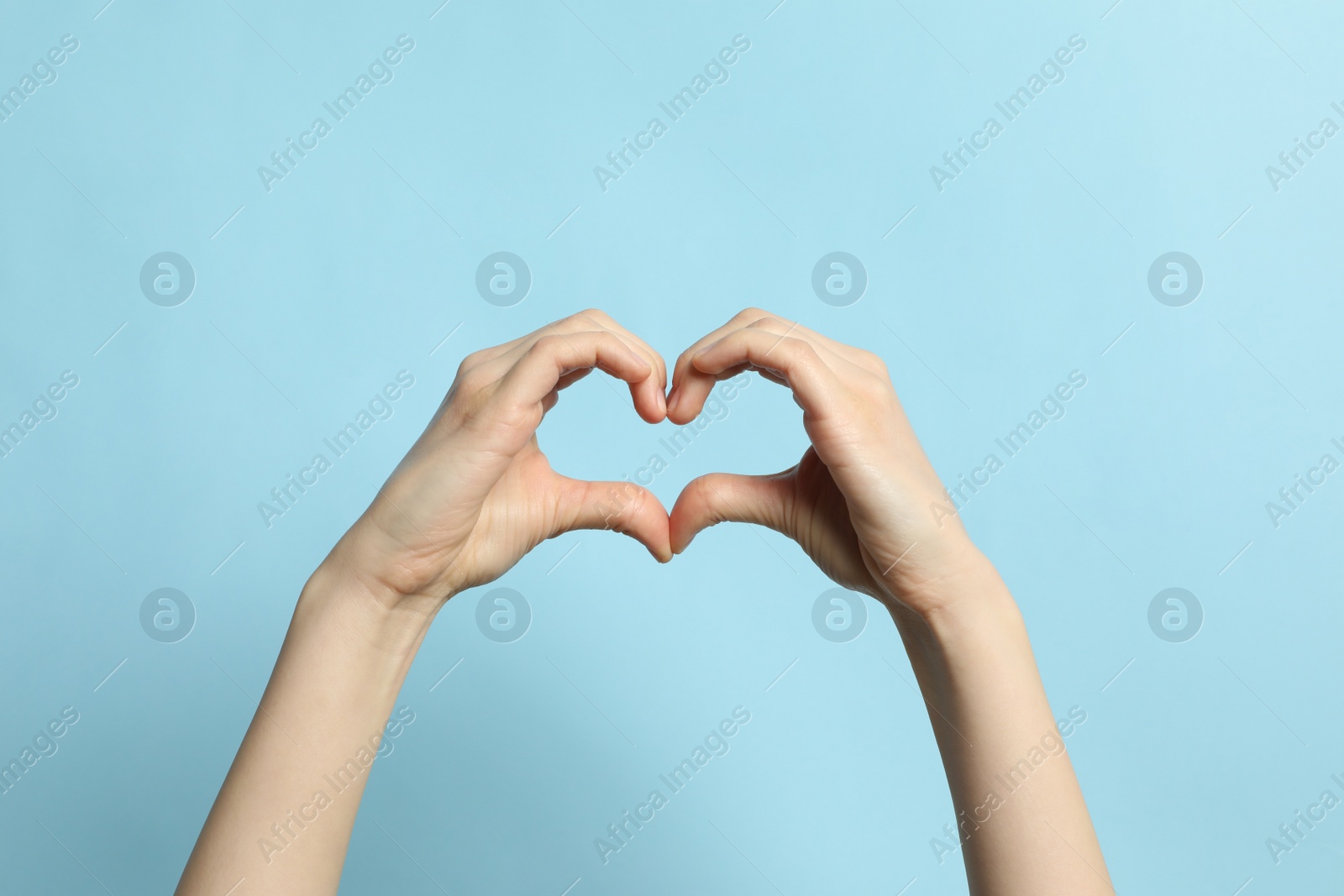Photo of Woman making heart with her hands on light blue background, closeup