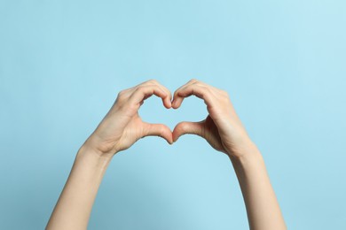 Photo of Woman making heart with her hands on light blue background, closeup