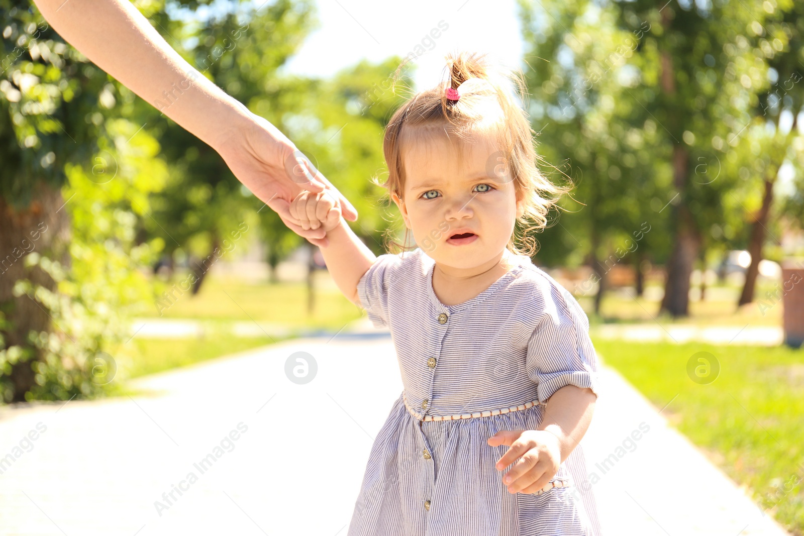 Photo of Adorable baby girl holding mother's hand while learning to walk outdoors