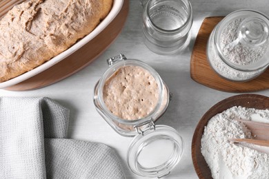 Sourdough starter in glass jar, flour, dough and water on light table, flat lay