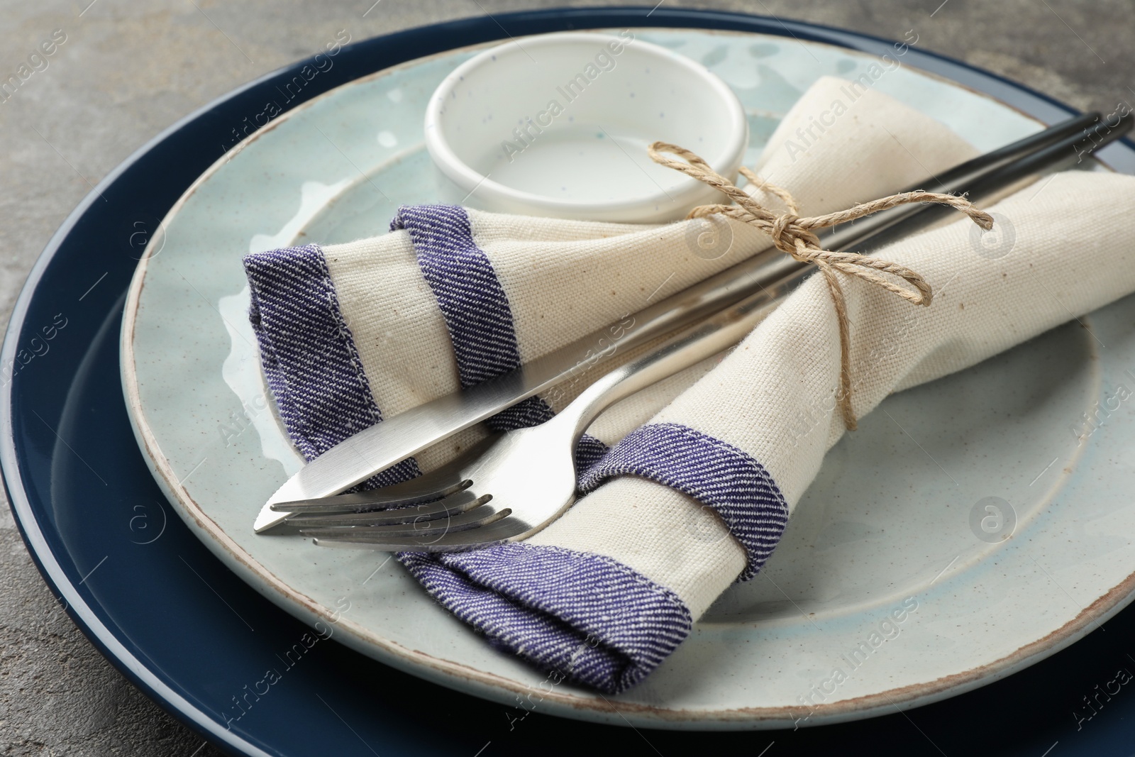 Photo of Stylish setting with cutlery, plates, bowl and napkin on grey table, closeup