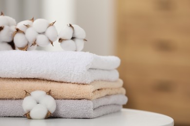 Photo of Terry towels and cotton branch with fluffy flowers on white table indoors, closeup. Space for text