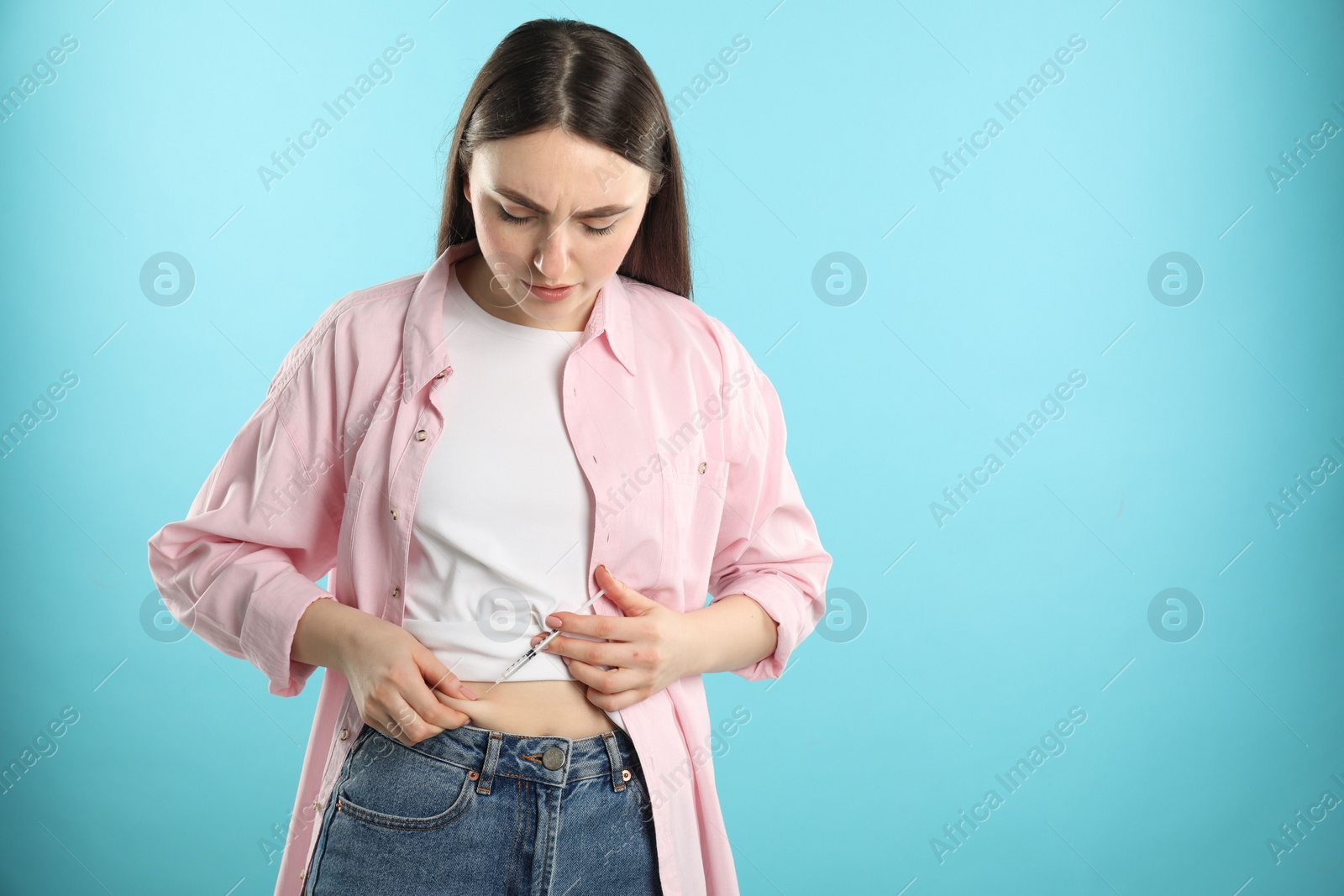 Photo of Diabetes. Woman making insulin injection into her belly on light blue background, space for text