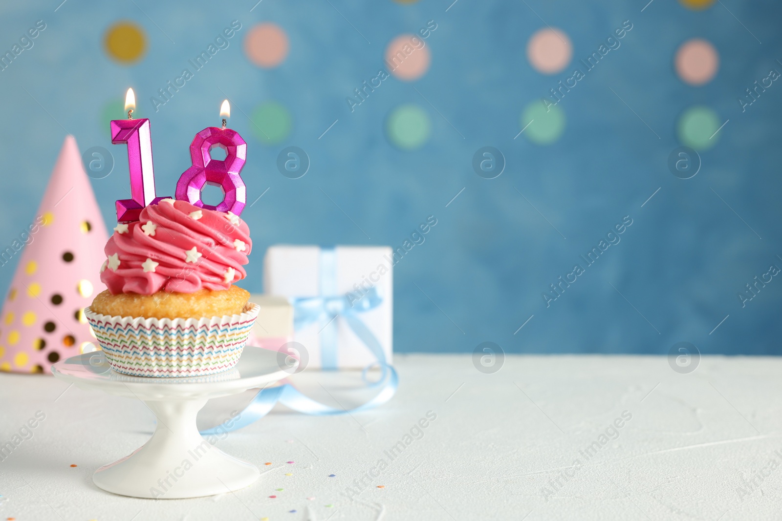 Photo of Coming of age party - 18th birthday. Delicious cupcake with number shaped candles on white table, space for text