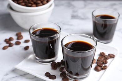 Glasses of coffee liqueur and beans on white marble table, closeup