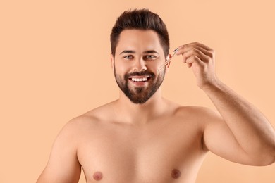 Photo of Handsome man applying cosmetic serum onto face on beige background