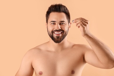 Handsome man applying cosmetic serum onto face on beige background