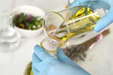 Scientist developing cosmetic oil at white table, closeup