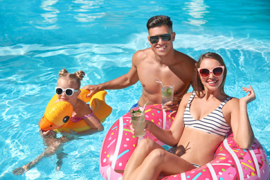 Happy family with inflatable rings and cocktails in outdoor swimming pool on sunny summer day