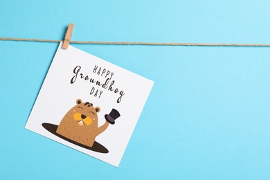 Photo of Happy Groundhog Day greeting card hanging on light blue background, space for text