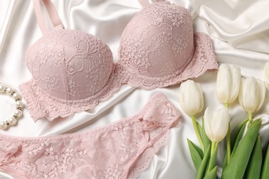 Photo of Composition with pink women's underwear and tulips on white fabric, closeup
