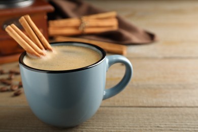 Photo of Cup of hot coffee with aromatic cinnamon on wooden table. Space for text