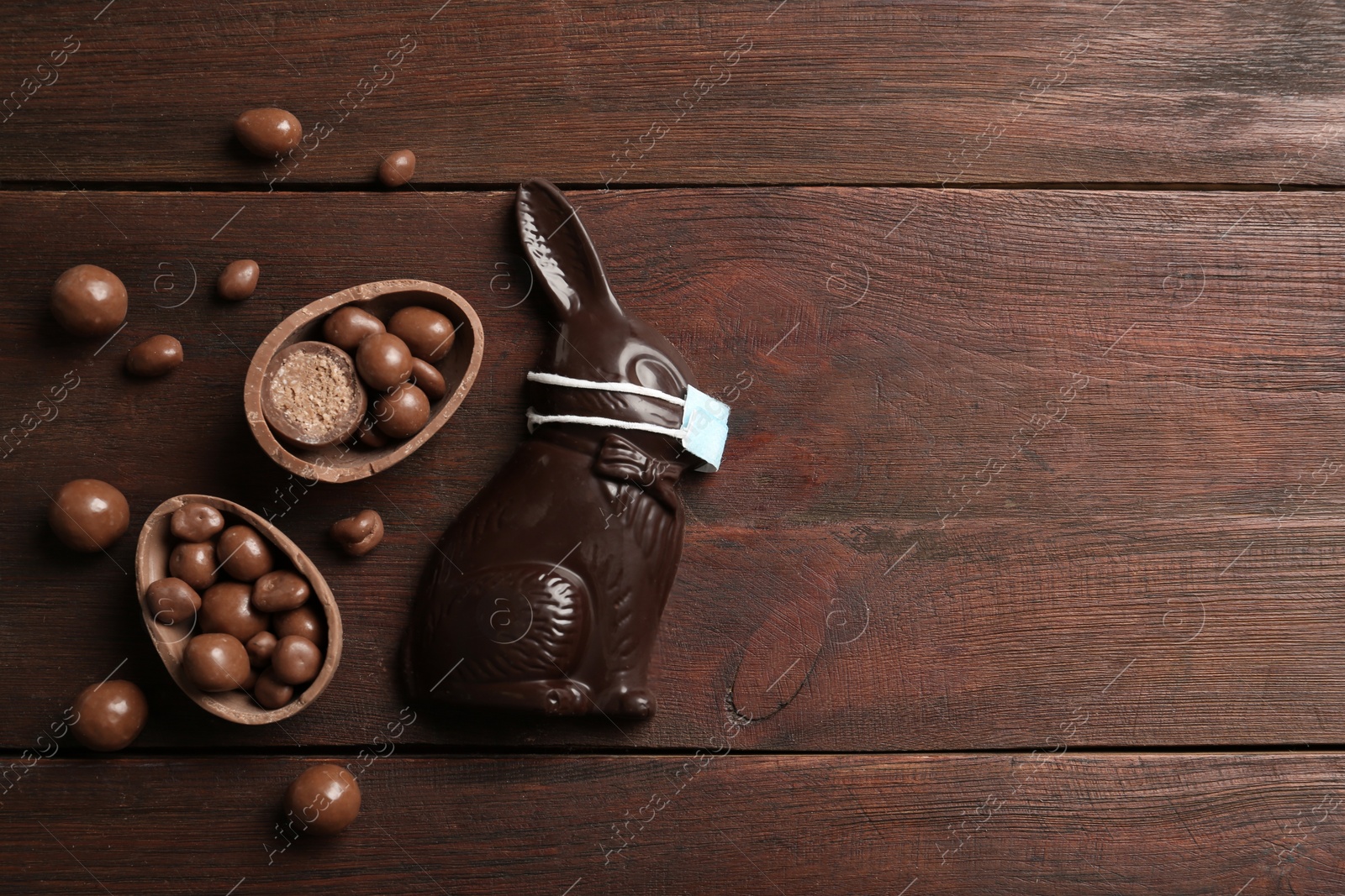 Photo of Chocolate bunny with protective mask, eggs and space for text on wooden table, flat lay. Easter holiday during COVID-19 quarantine