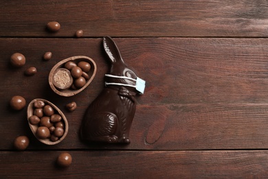 Photo of Chocolate bunny with protective mask, eggs and space for text on wooden table, flat lay. Easter holiday during COVID-19 quarantine