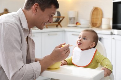 Photo of Father feeding his cute little baby in kitchen