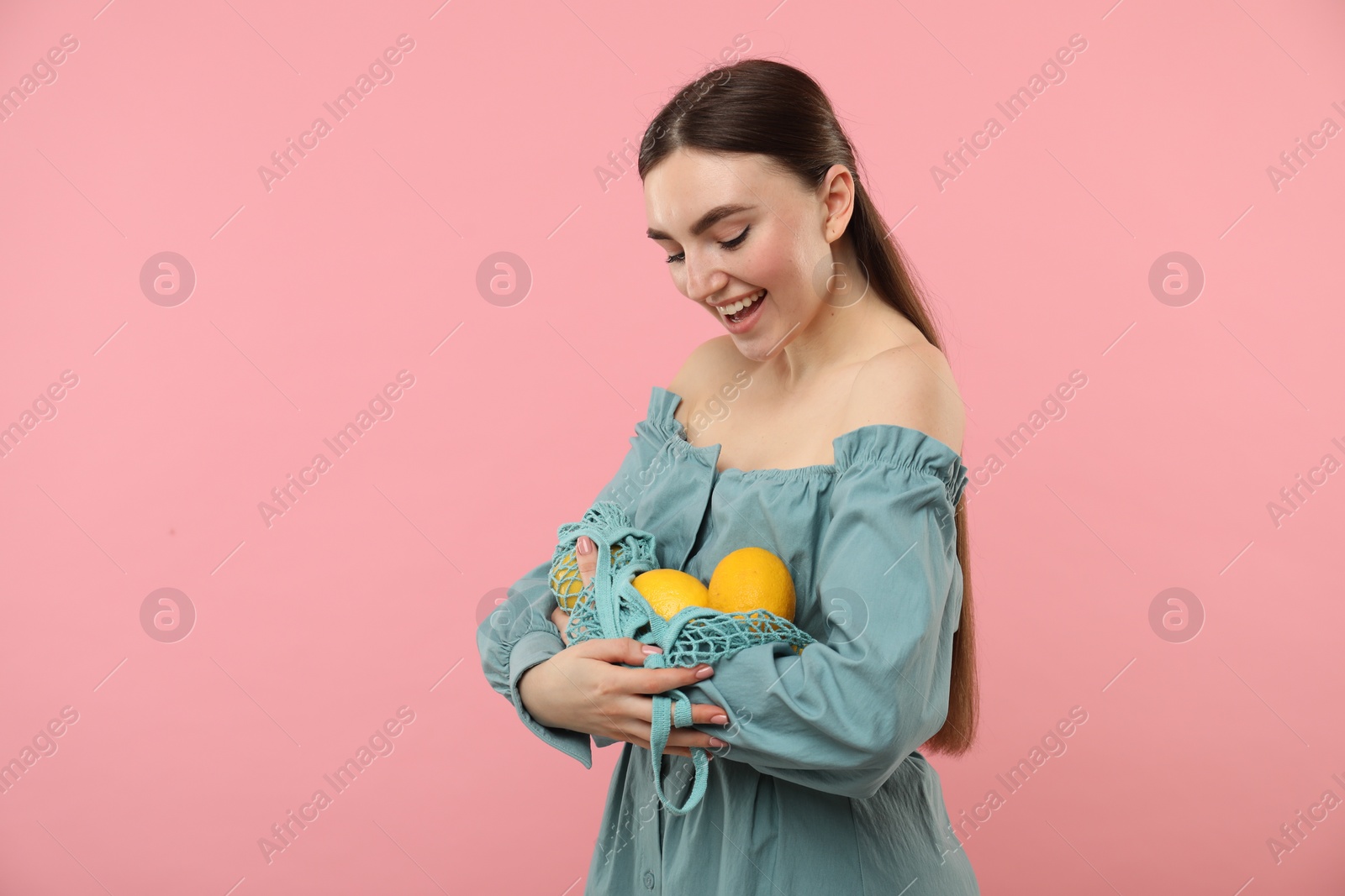 Photo of Woman with string bag of fresh lemons on pink background, space for text