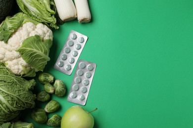 Photo of Blisters of pills and foodstuff on green background, flat lay with space for text. Prebiotic supplements