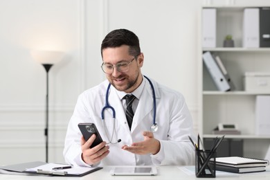 Doctor having online consultation via smartphone at table in clinic