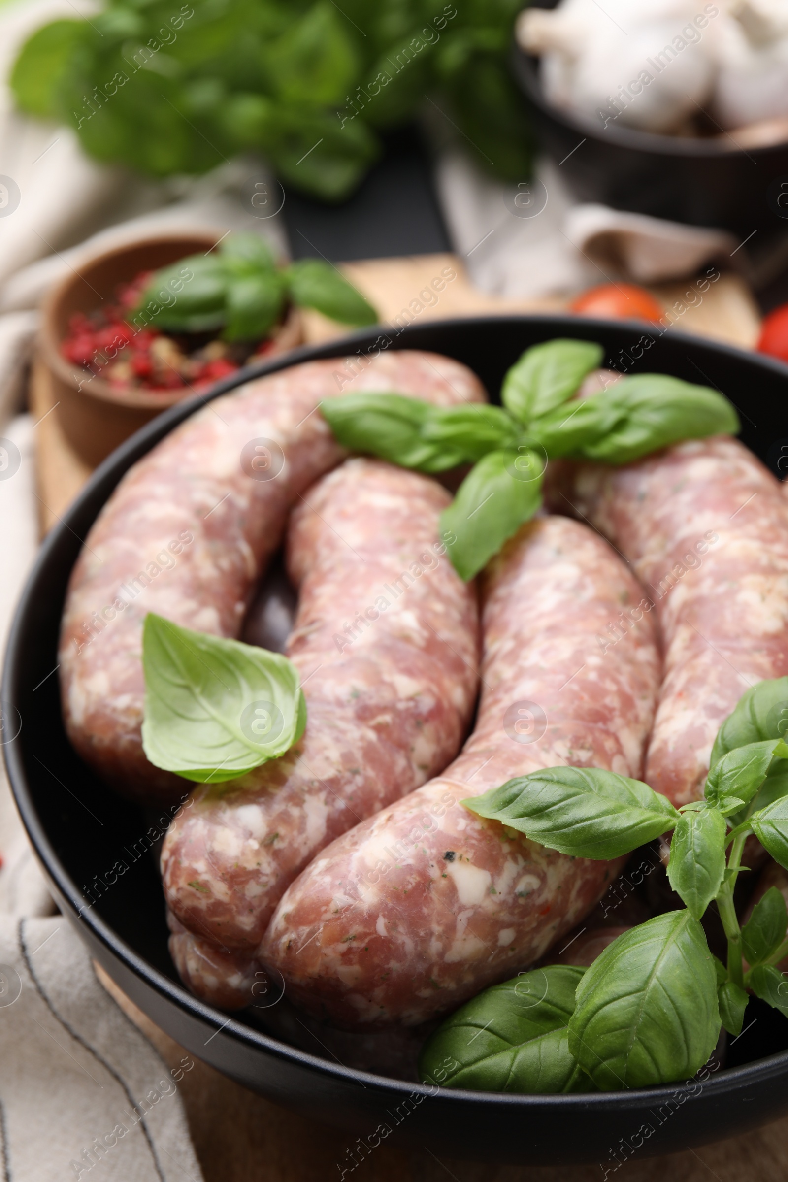 Photo of Raw homemade sausages and basil leaves on table, closeup