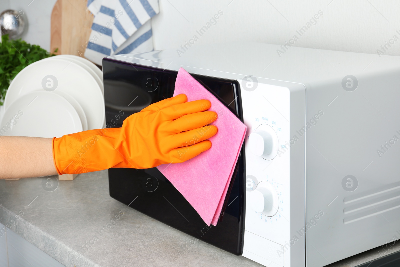 Photo of Woman cleaning microwave oven with rag in kitchen, closeup