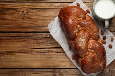 Photo of Delicious yeast dough cake, nuts and cup of milk on wooden table, flat lay. Space for text