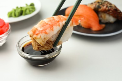 Photo of Dipping tasty sushi into soy sauce at white table, closeup. Space for text