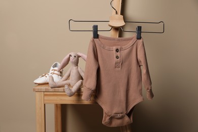 Photo of Baby bodysuit, shoes and toy bunny on chair near beige wall