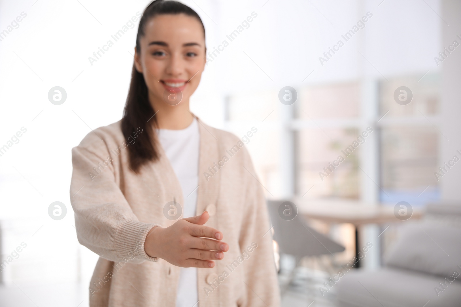 Photo of Happy young woman offering handshake indoors, focus on hand. Space for text