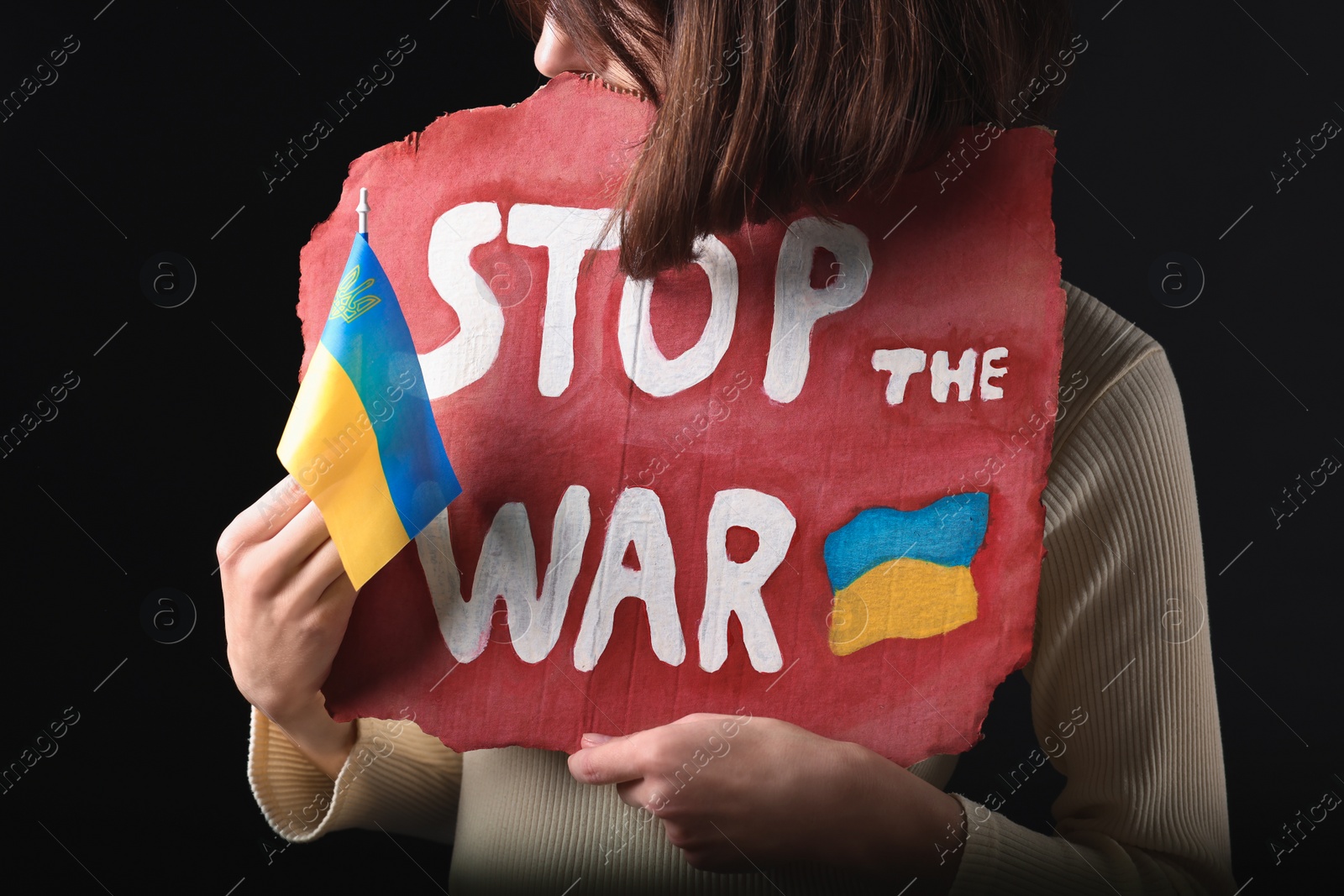 Photo of Woman holding poster with words Stop the War and Ukrainian flag on black background