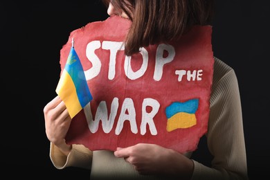 Photo of Woman holding poster with words Stop the War and Ukrainian flag on black background