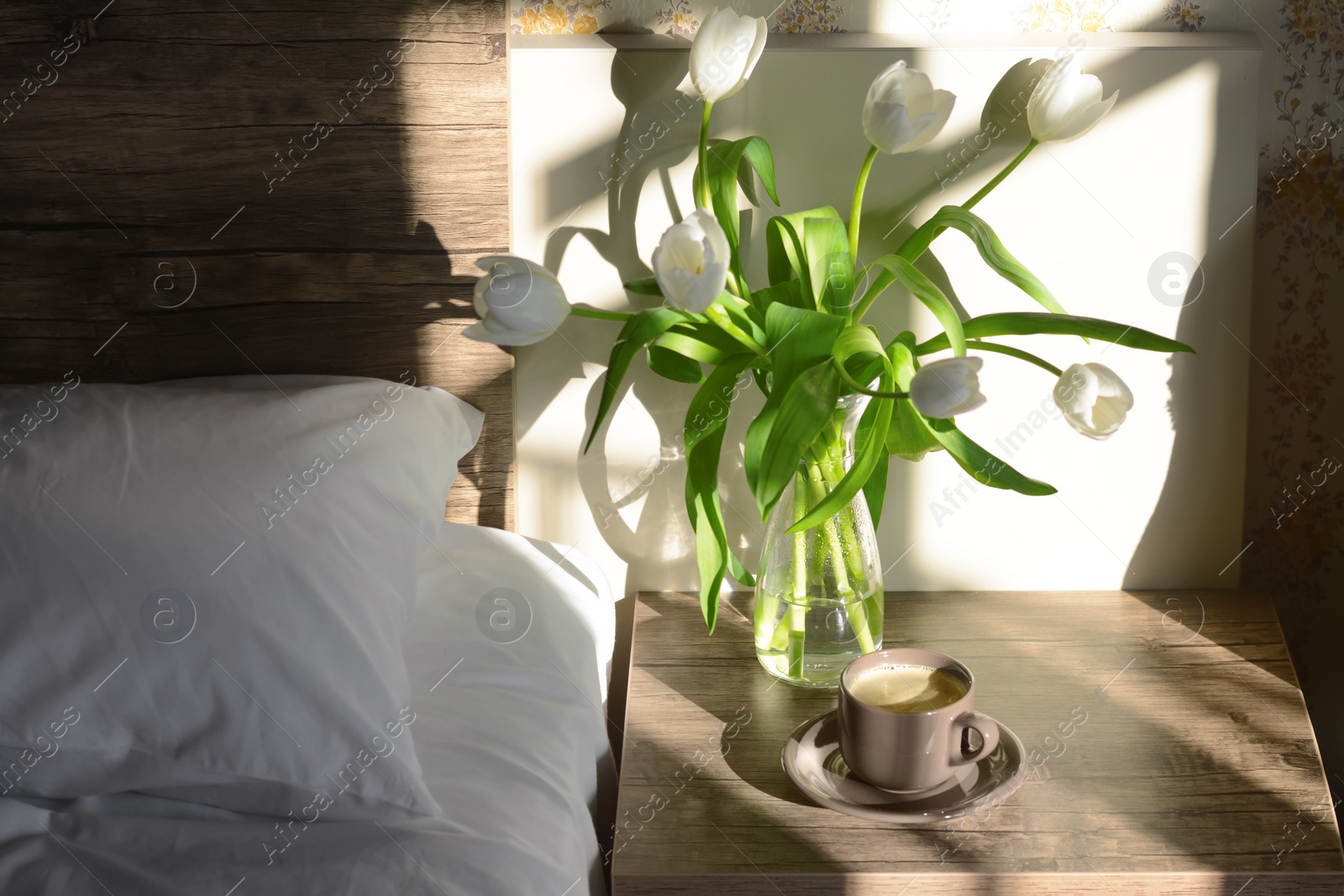 Photo of Beautiful white tulip bouquet and cup of coffee on nightstand in bedroom