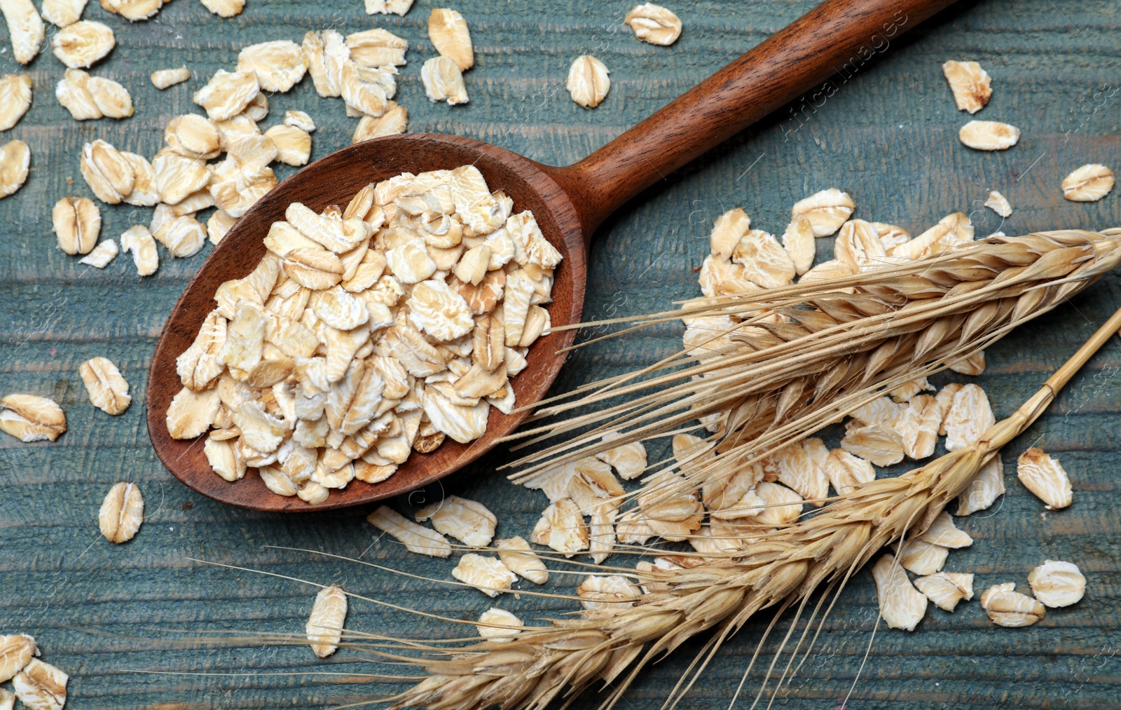 Photo of Spoon with oatmeal and spikelets on light blue wooden table, flat lay