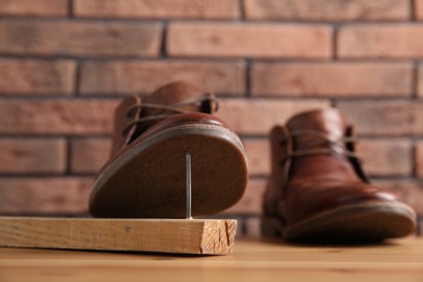 Metal nail in wooden plank and shoes on table