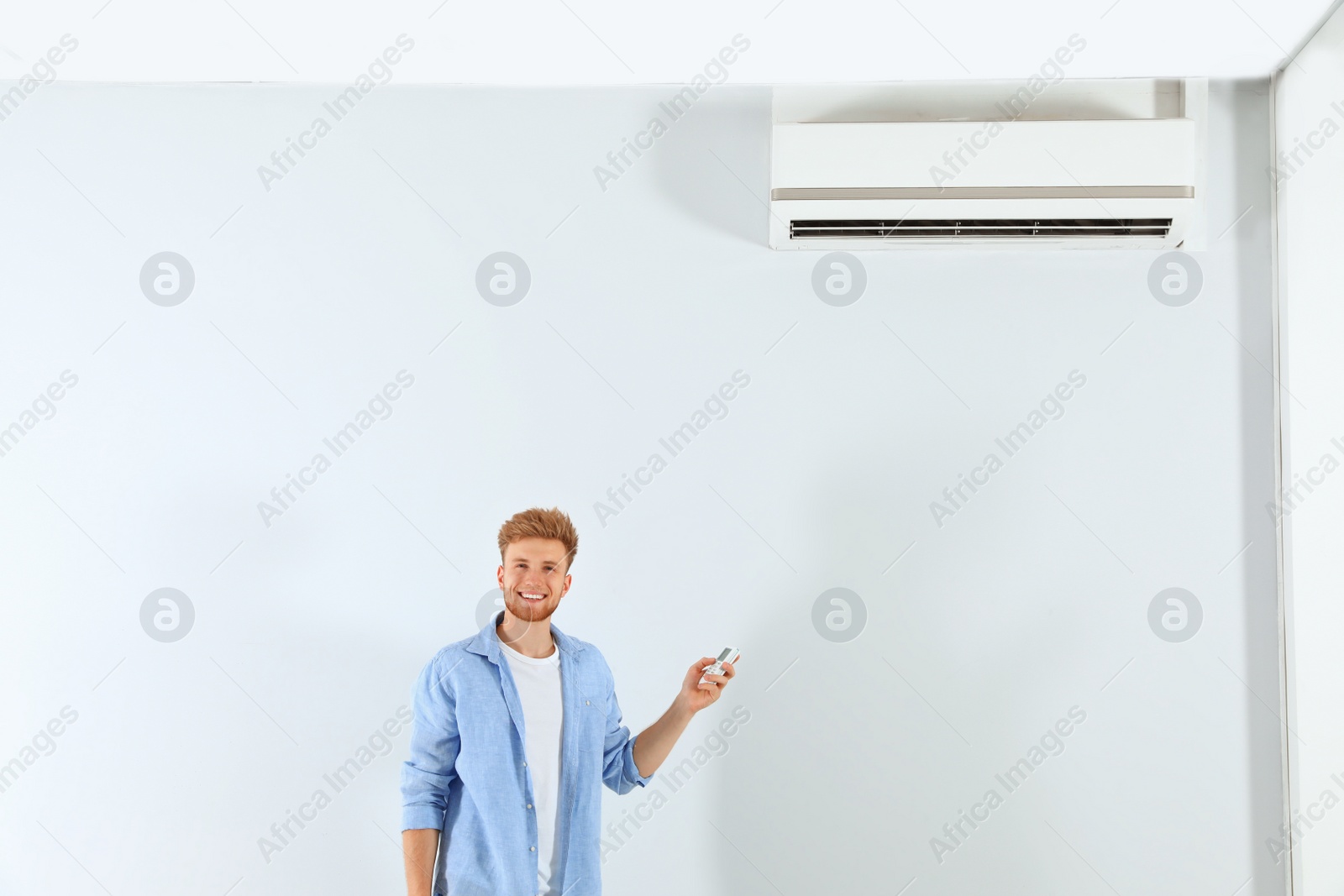 Photo of Young man operating air conditioner with remote control indoors. Space for text