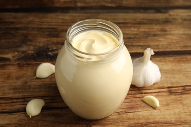 Photo of Jar of delicious mayonnaise and fresh garlic on wooden table