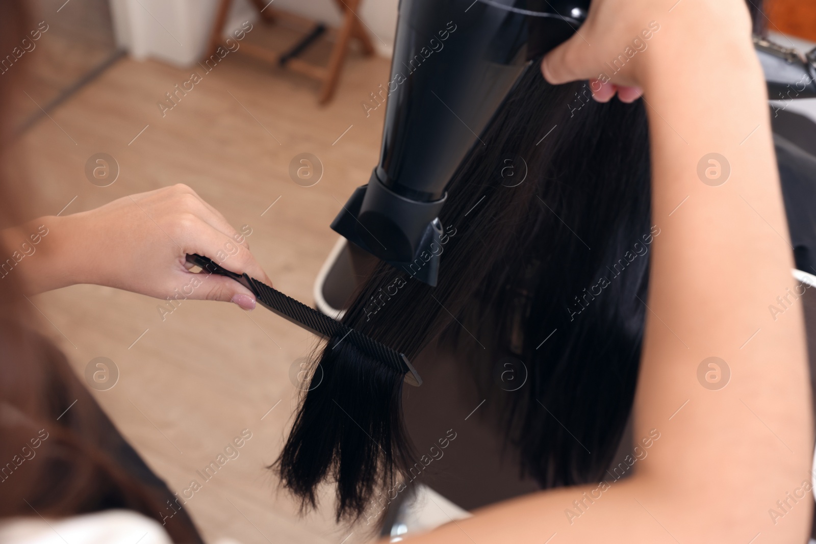 Photo of Hairdresser drying woman's hair in beauty salon, closeup