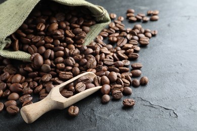 Photo of Bag and wooden scoop with roasted coffee beans on black table, closeup. Space for text