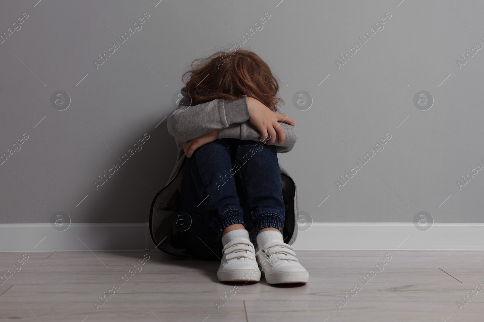 Photo of Child abuse. Upset boy sitting on floor near grey wall