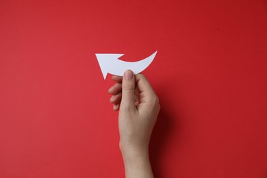 Woman holding curved paper arrow on red background, top view