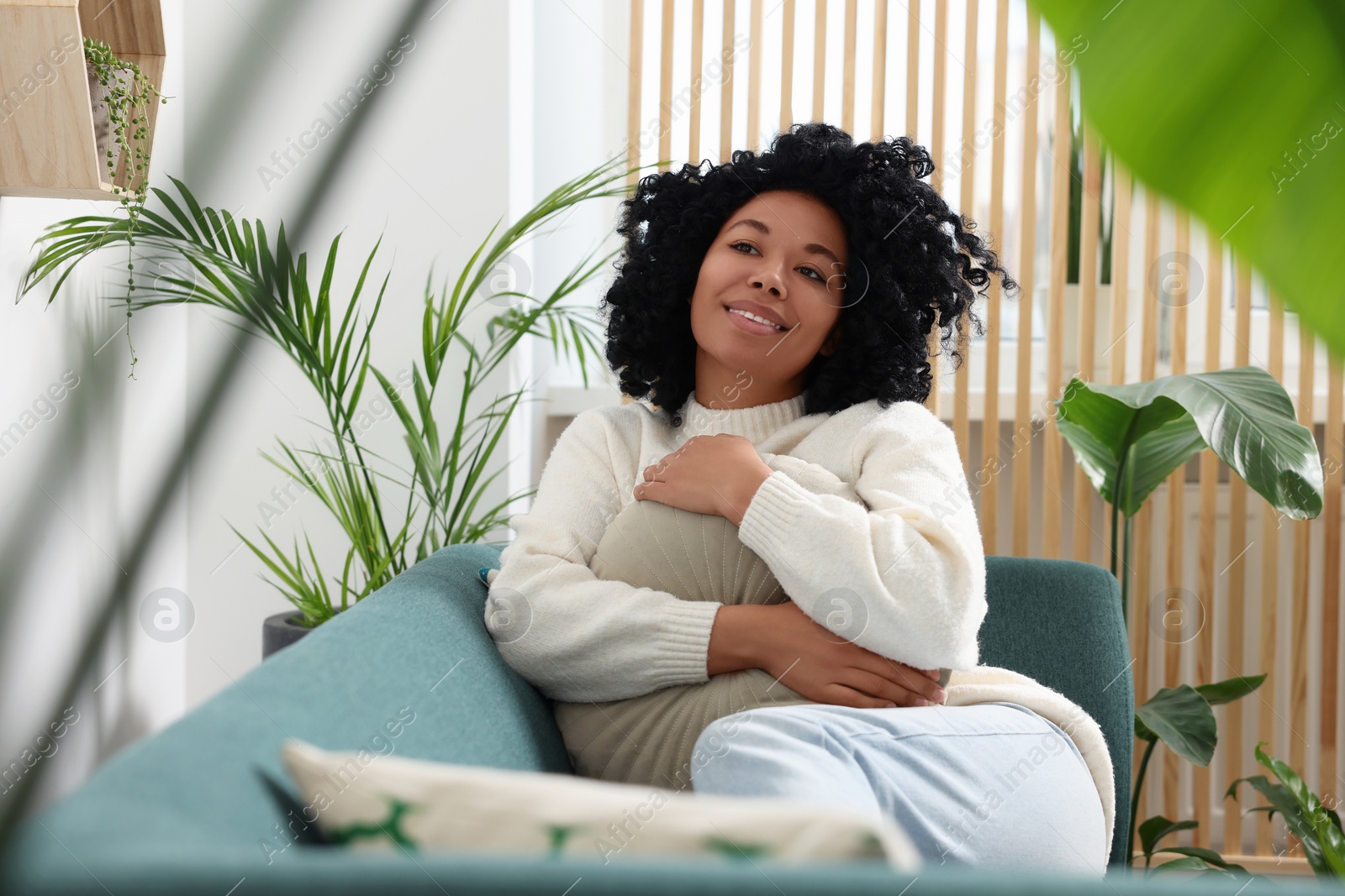 Photo of Happy woman relaxing on sofa near beautiful houseplants at home