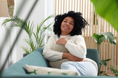 Photo of Happy woman relaxing on sofa near beautiful houseplants at home