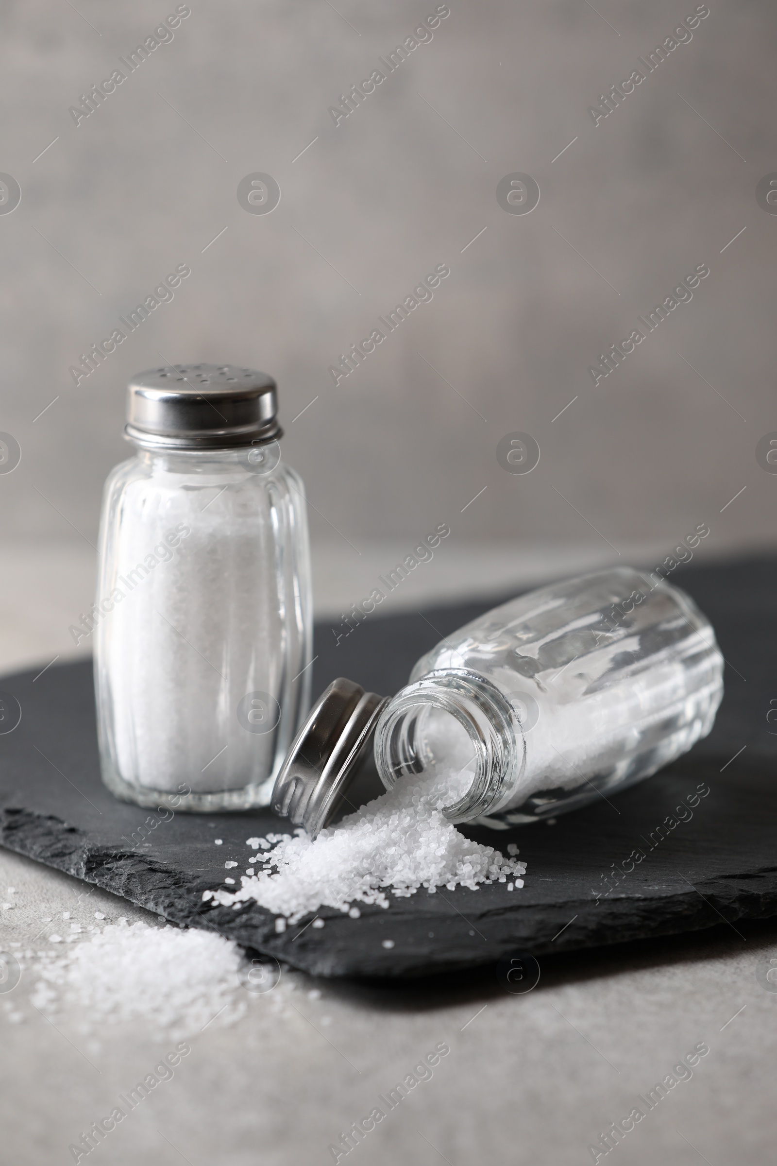 Photo of Natural salt in shakers on grey table, closeup