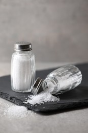 Photo of Natural salt in shakers on grey table, closeup