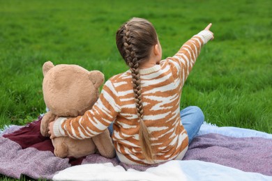 Photo of Little girl with teddy bear on plaid outdoors, back view