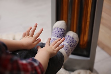 Little kid warming near electric heater at home, closeup