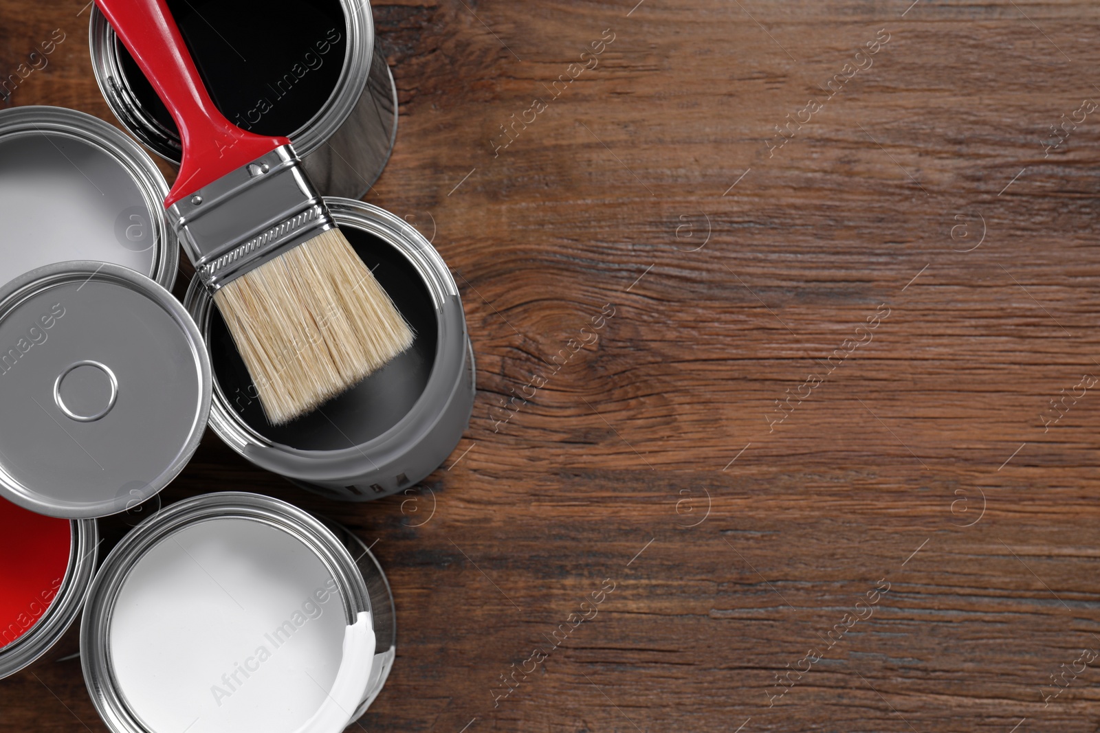 Photo of Cans of paints and brush on wooden table, flat lay. Space for text