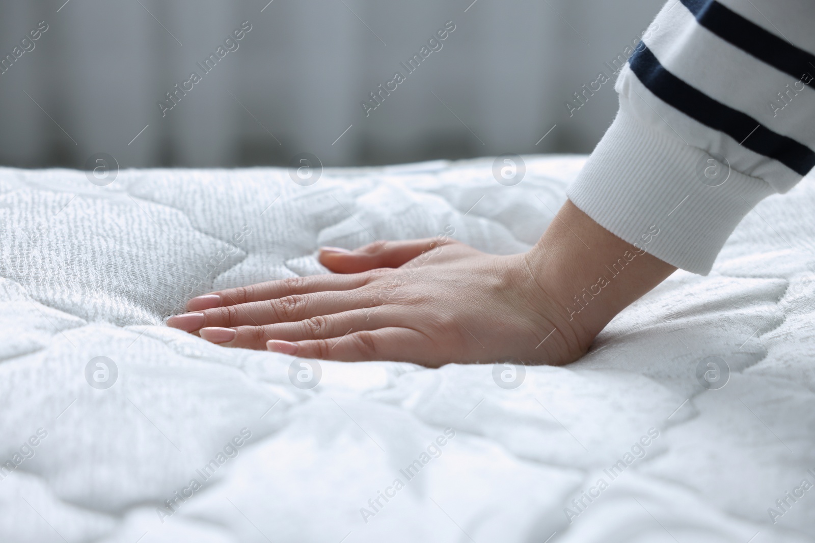 Photo of Woman touching soft white mattress indoors, closeup