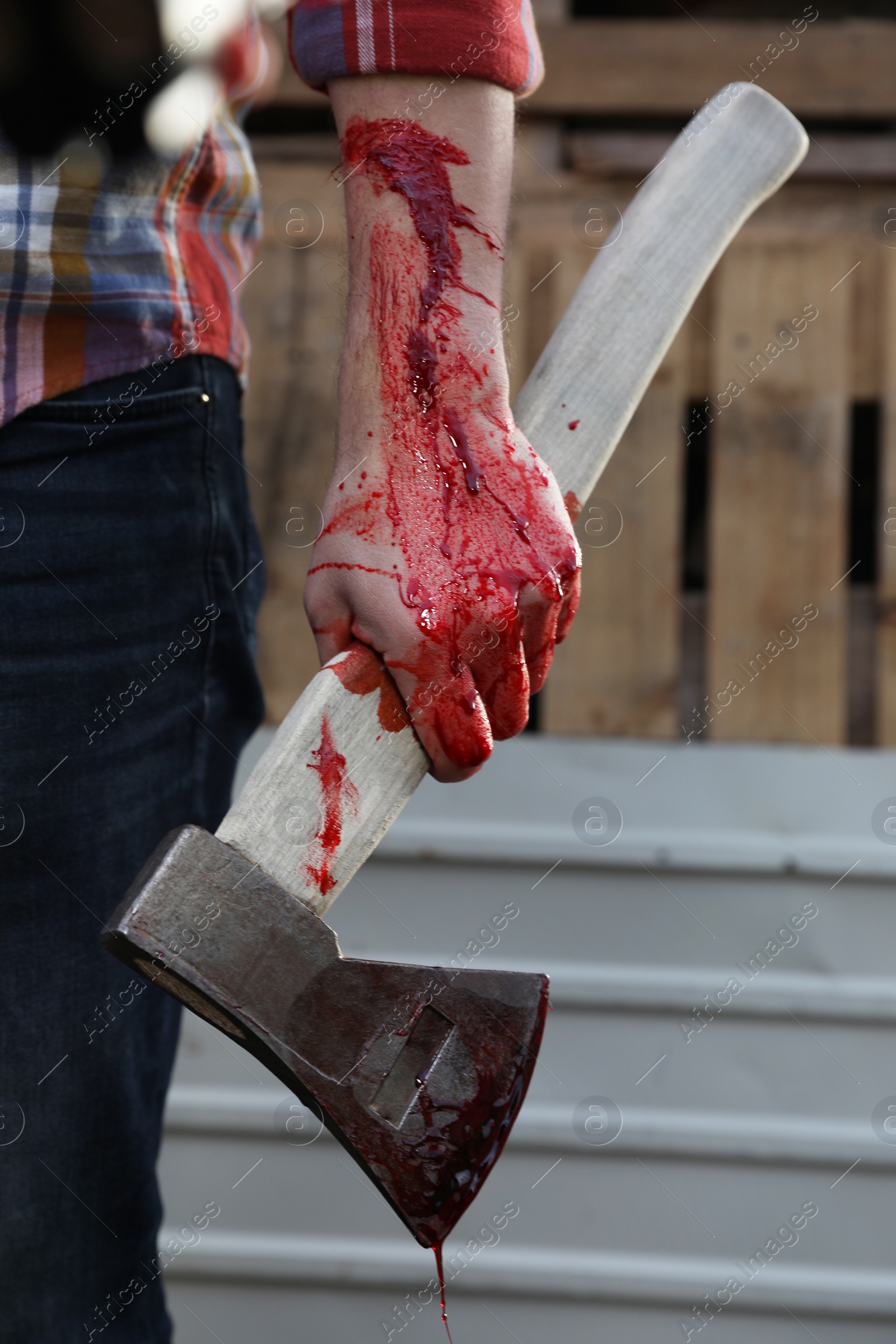 Photo of Man holding bloody axe outdoors, closeup view